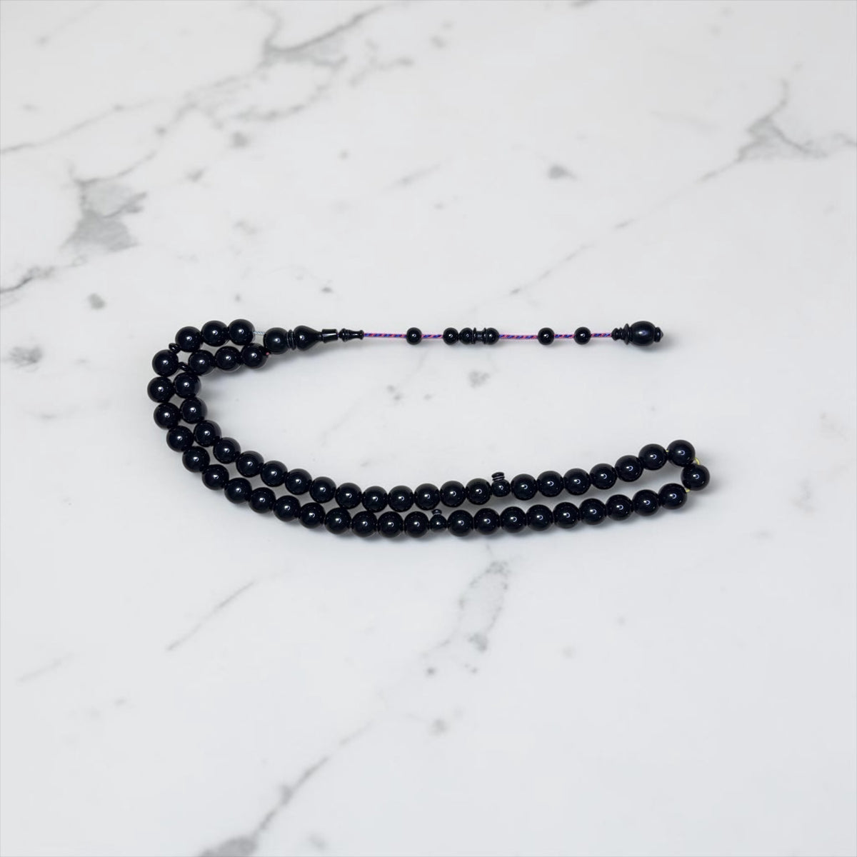 Miraj store handcrafted black Bakelite prayer beads with 51 polished 11mm beads and a decorative tassel on marble.